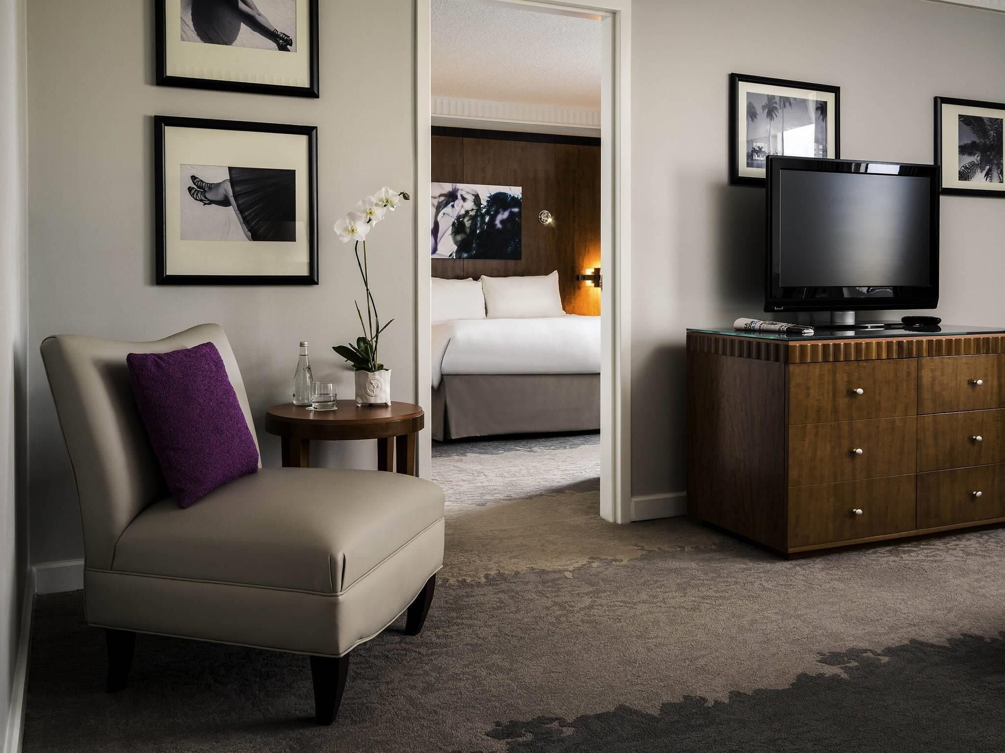 A hotel room with a bed, a TV, a sofa, a dresser, and framed pictures on the walls.