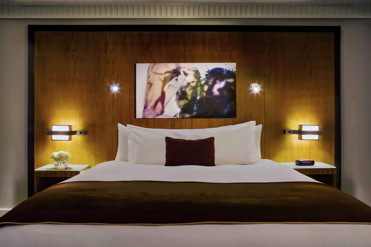 A hotel room with a large bed, two bedside tables with lamps, and a painting above the bed.