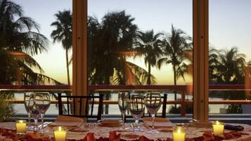 Una mesa dispuesta para cenar, con velas, copas y pétalos de rosa, con vistas a palmeras.