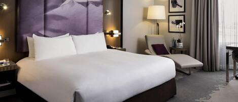 A hotel room with a large bed, a chair, a desk, and a lamp.