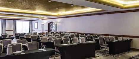 A conference room with rows of chairs, tables, and a projector screen.
