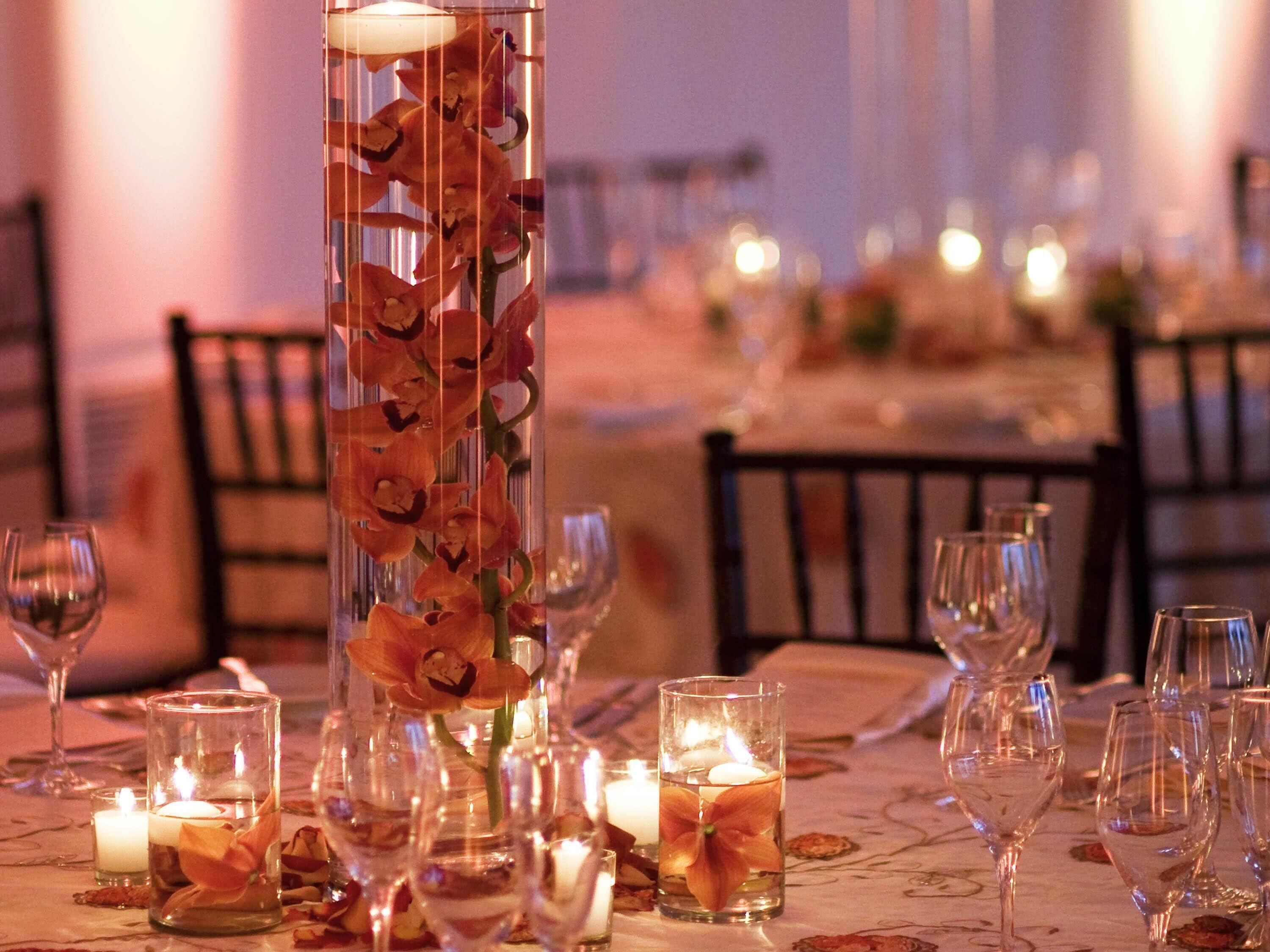 A table set for dining with candles, glasses, and a tall vase with flowers.