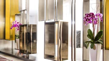 A modern lobby with reflective glass panels, a patterned carpet, and potted plants.