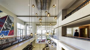 A spacious hotel lobby with a high ceiling, hanging pendant lights, a central seating area, and a large mural on the wall. - Pullman Miami Airport (Miami)
