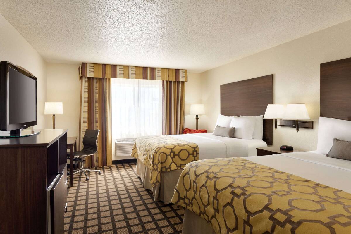 A hotel room with two beds, a desk with a television, and a chair.