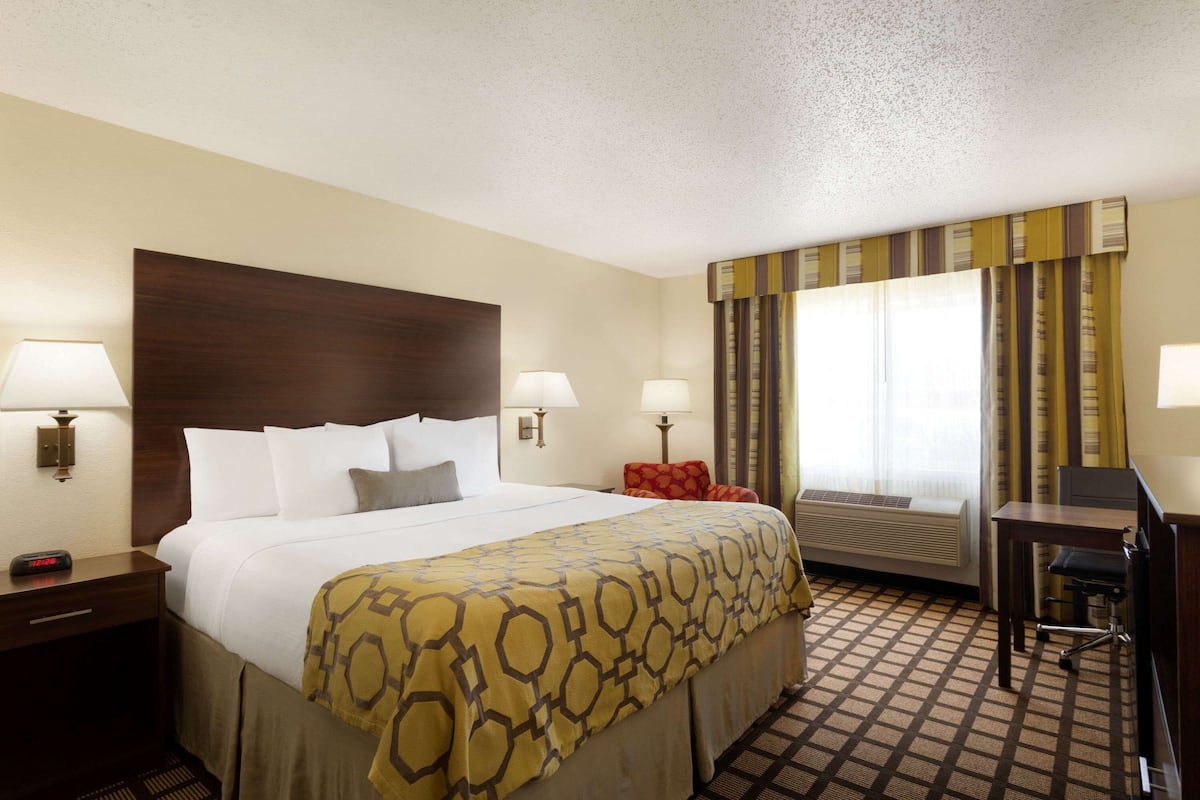 A hotel room with a large bed, two bedside lamps, a desk with a chair, a window with curtains, and a wall-mounted heater.