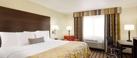 A hotel room with a large bed, two bedside lamps, a desk with a chair, and an air conditioning unit.
