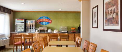 A breakfast area with wooden tables and chairs, a coffee machine, and a breakfast counter with various food items.