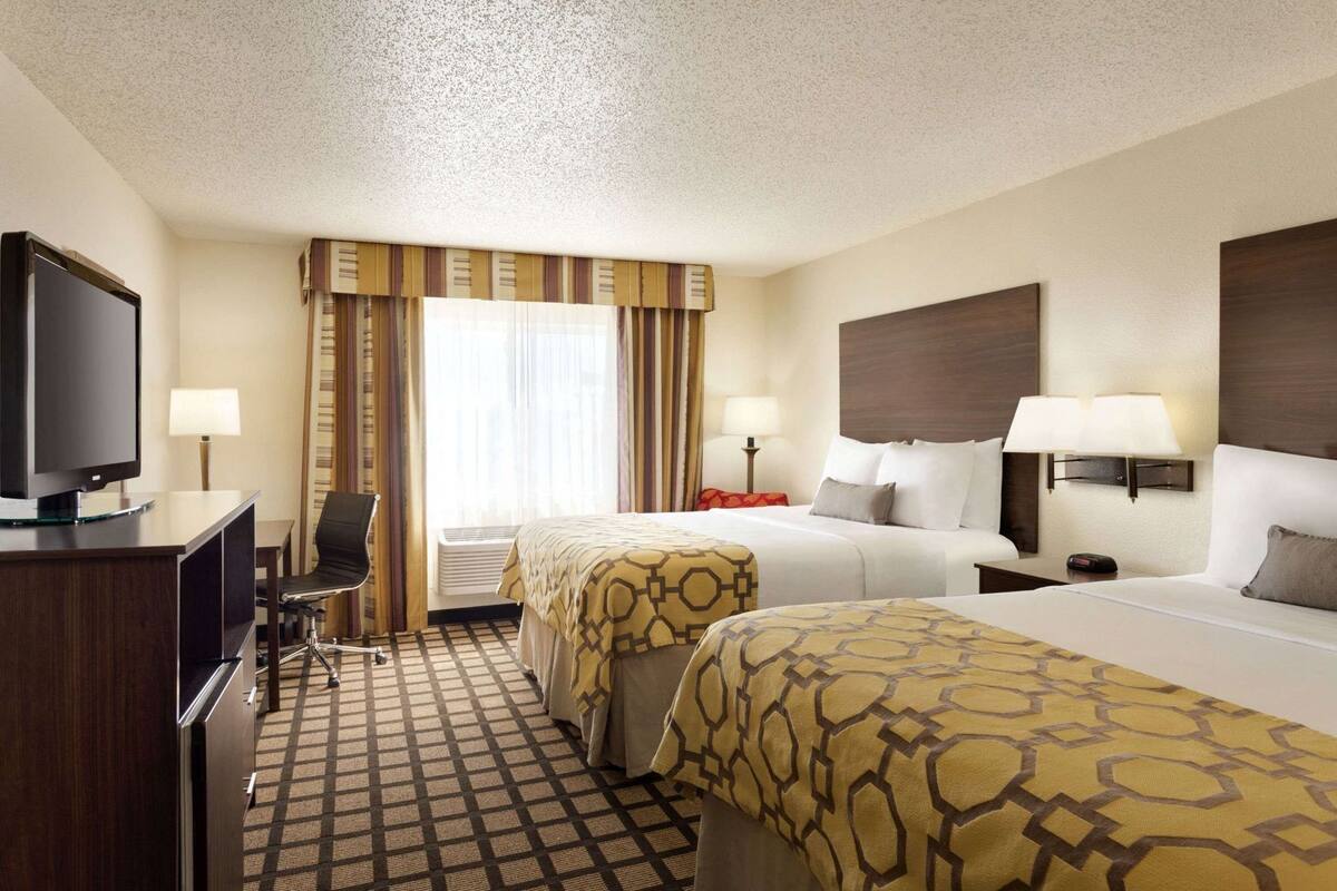 A hotel room with two beds, a desk with a television, a chair, and a window with curtains.