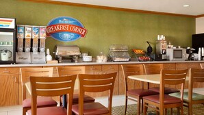 A breakfast area with a sign for 'Baymont Breakfast Corner', a coffee machine, cereal boxes, and a fruit display. - Baymont by Wyndham Salina (Salina)