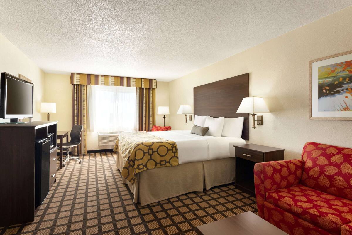 A hotel room with a bed, a desk, a TV, a sofa, and a painting on the wall.