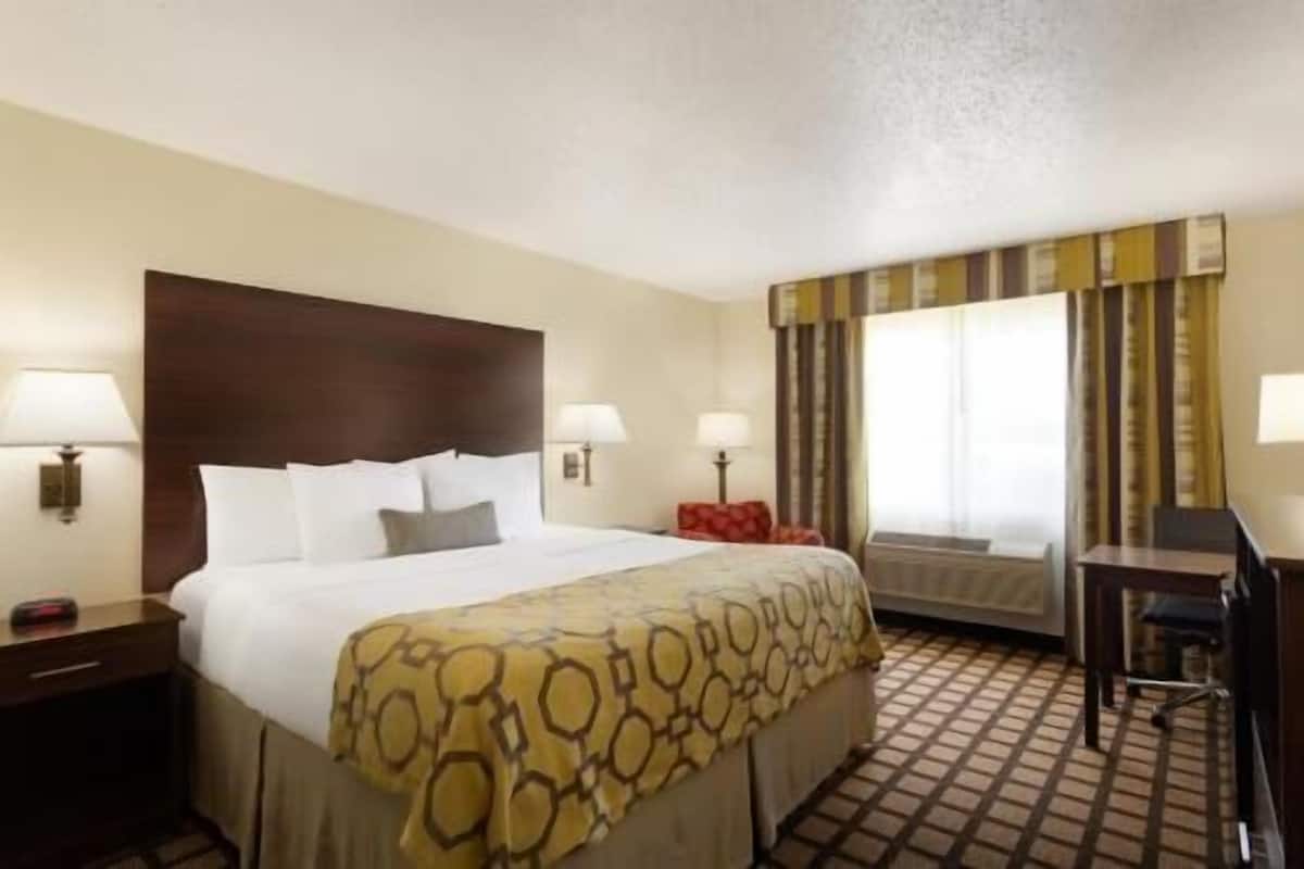 A hotel room with a bed, two bedside lamps, a desk, and a window with curtains.