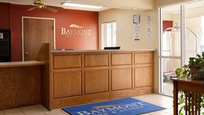 A reception area with a wooden reception desk, a Baymont Inn & Suites logo, a blue doormat, and a ceiling fan. - Baymont by Wyndham Salina (Salina)