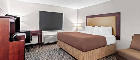 Una habitación de hotel con cama, escritorio, silla, lámpara y un amplio ventanal.
