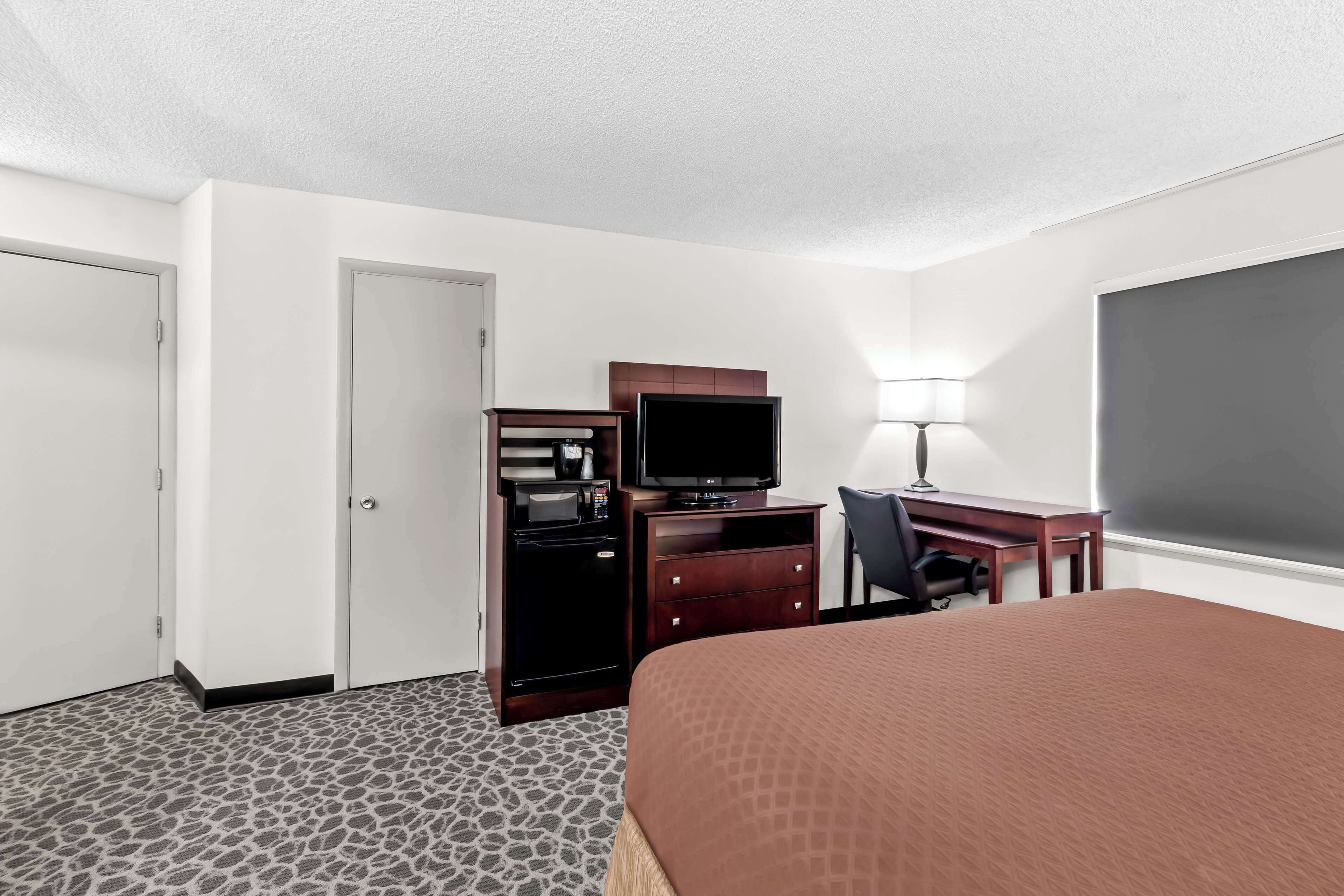 Une chambre d’hôtel comprenant un lit, un bureau avec un ordinateur, une télévision et une armoire.