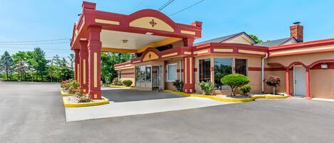 A motel with a red and beige facade, a covered entrance, and a parking lot.