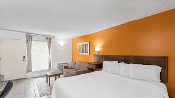 Una habitación de hotel con cama, escritorio, silla, mesita y ventana con cortinas.