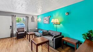 Sala de estar com parede azul-turquesa, piso de madeira, sofá, poltrona, mesa e luminária.