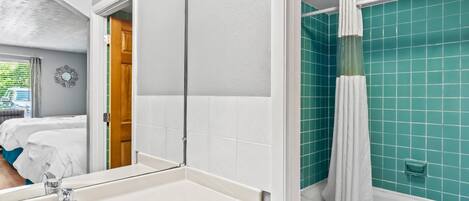 A bathroom with a white sink, a mirror, a shower with a white curtain, and teal tiled walls.