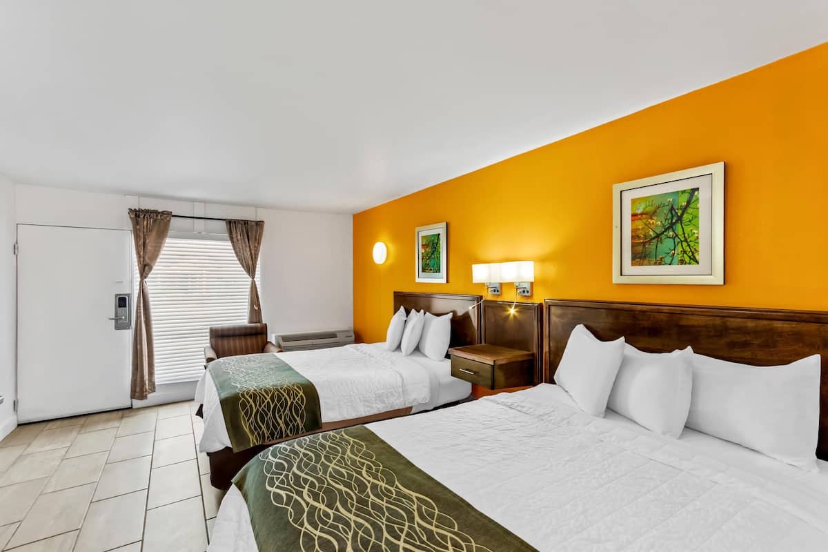 A hotel room with two beds, a window with curtains, a wall-mounted clock, and a framed picture.