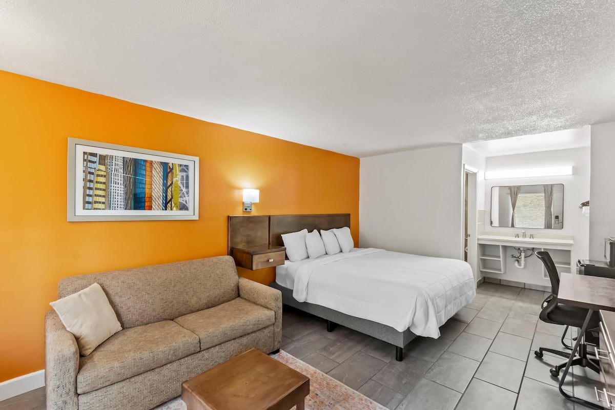 A hotel room with a bed, a sofa, a desk, and a bathroom.