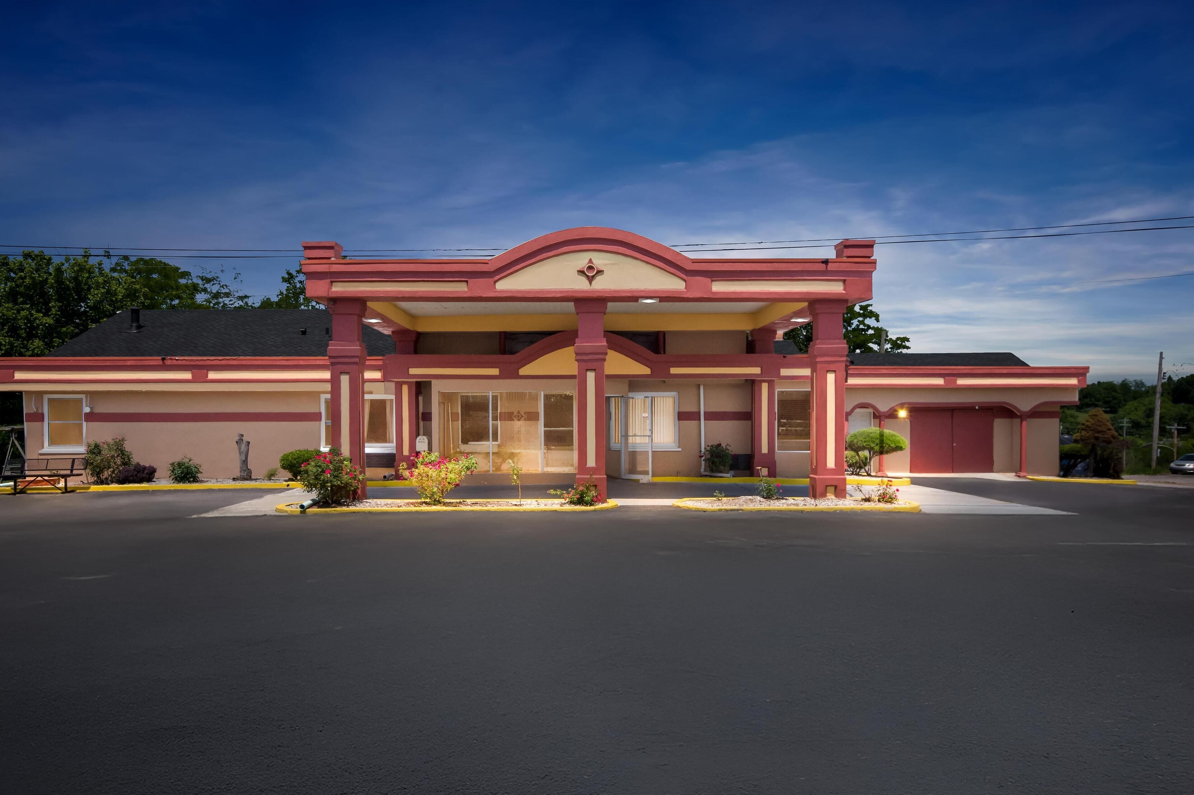 A building with a red and beige facade, a central entrance with a decorative arch, and a parking lot in front.