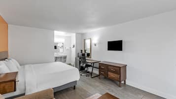 A hotel room with a bed, a desk, a chair, a dresser, a TV, and a bathroom visible in the background.
