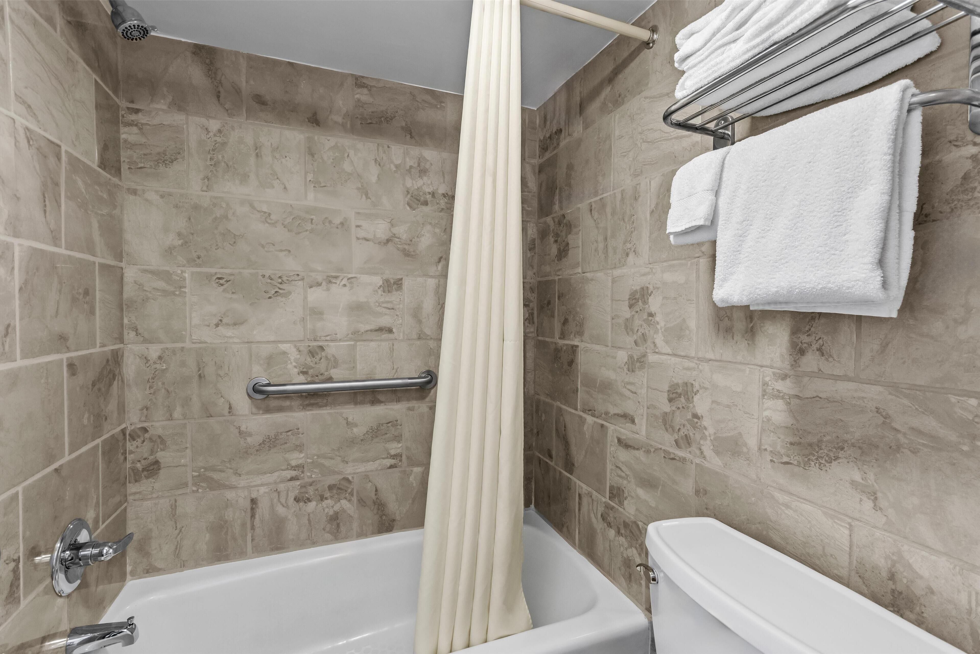 Un baño con bañera, cortina de ducha, toallero con toallas y baranda.