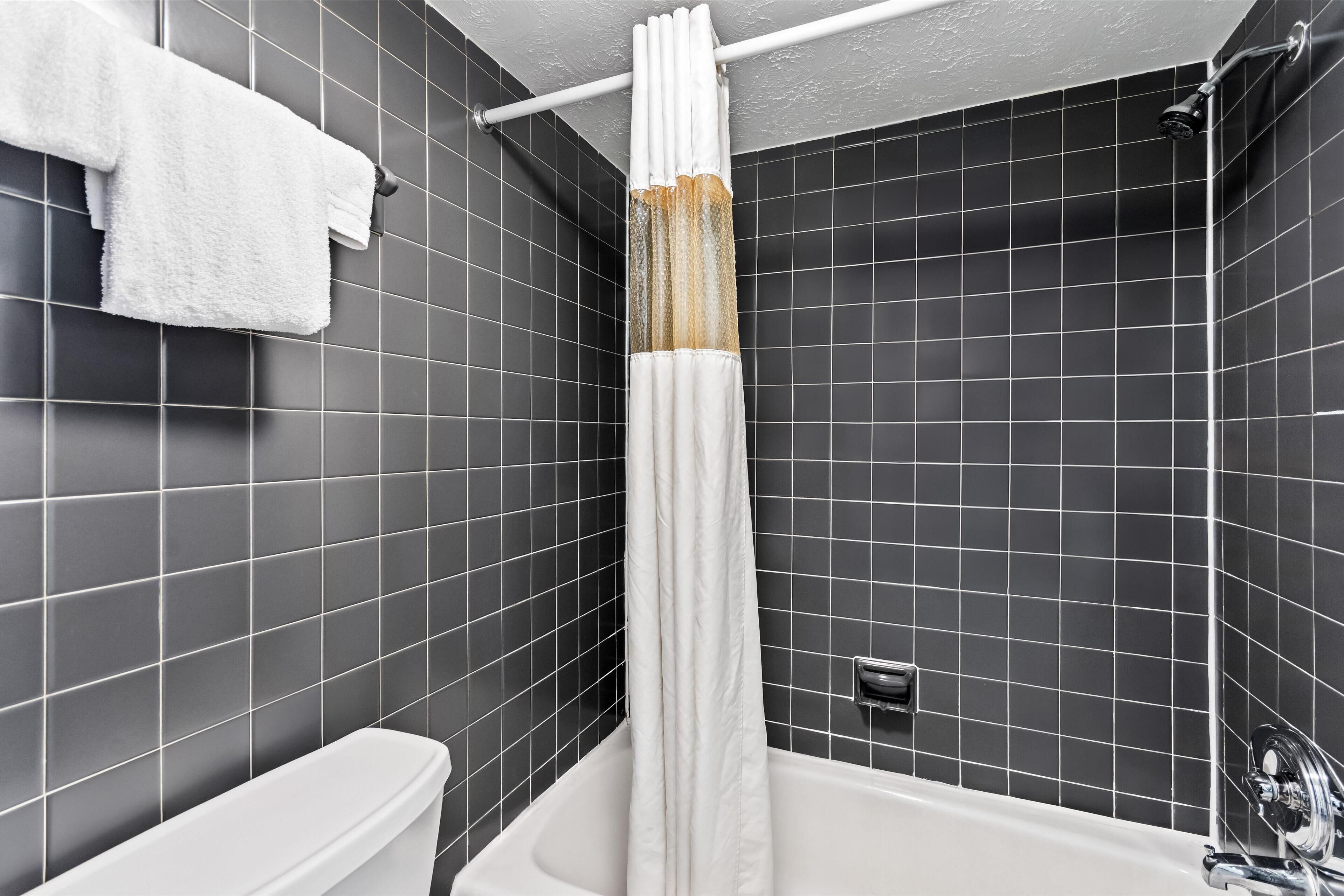 A modern bathroom with a white bathtub, a shower curtain, and a toilet.
