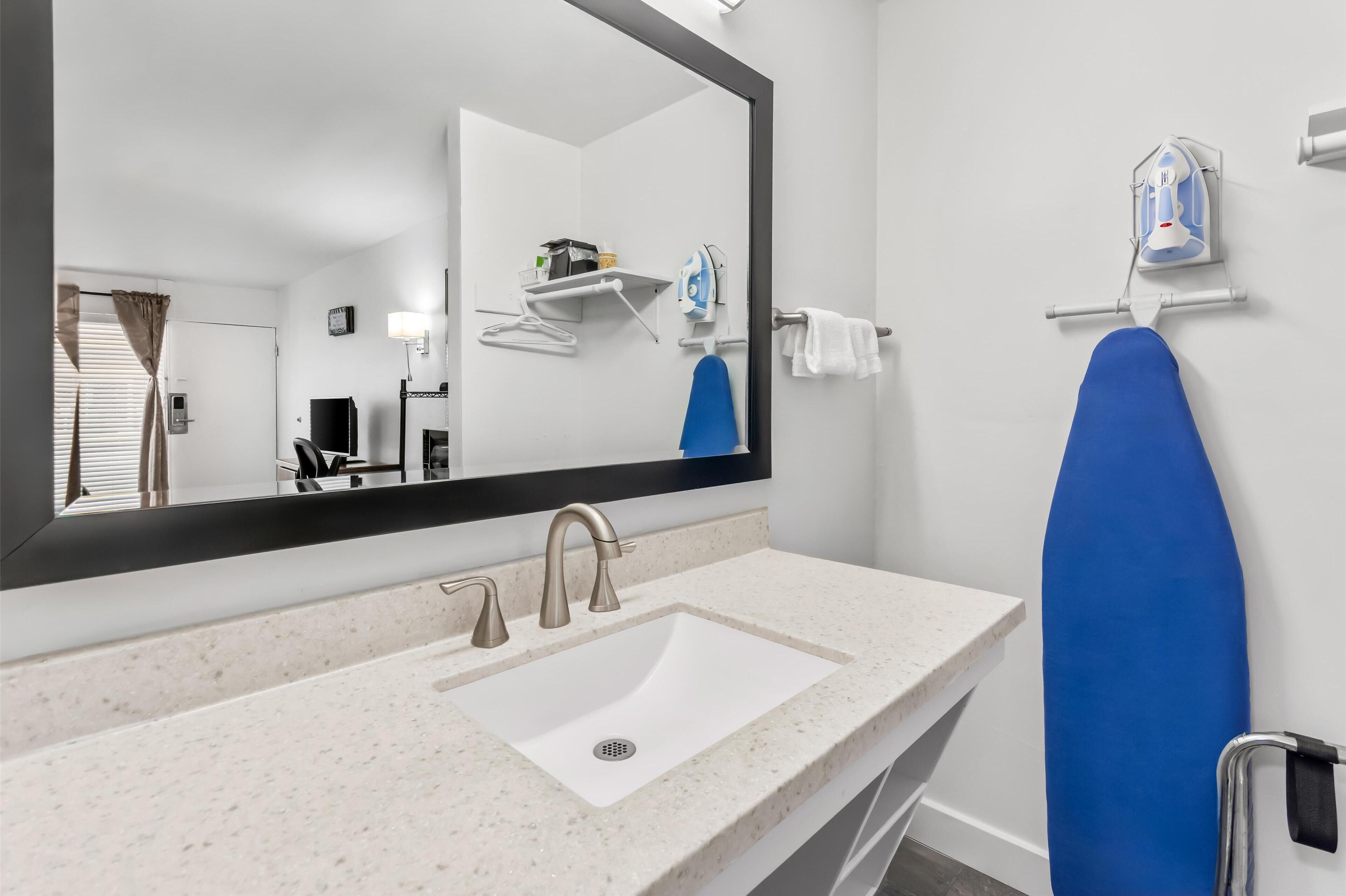 A bathroom with a white sink, a large mirror, and a blue ironing board.