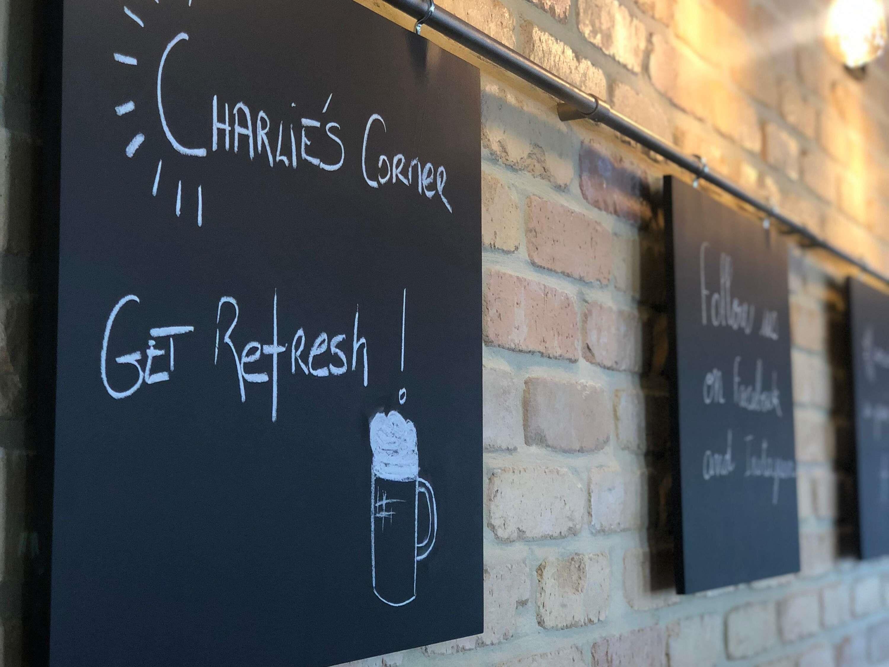 A wall with chalkboards displaying 'CHARLIE'S CORNER' and 'GET REFRESH!' with a drawing of a mug.