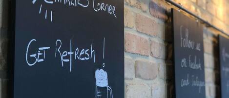 Una pared con pizarras que muestran 'CHARLIE'S CORNER' y '¡REFRÉSCATE!' con un dibujo de una taza.