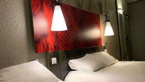 Une chambre d’hôtel avec un lit, des oreillers blancs, une tête de lit en bois et deux lampes suspendues.