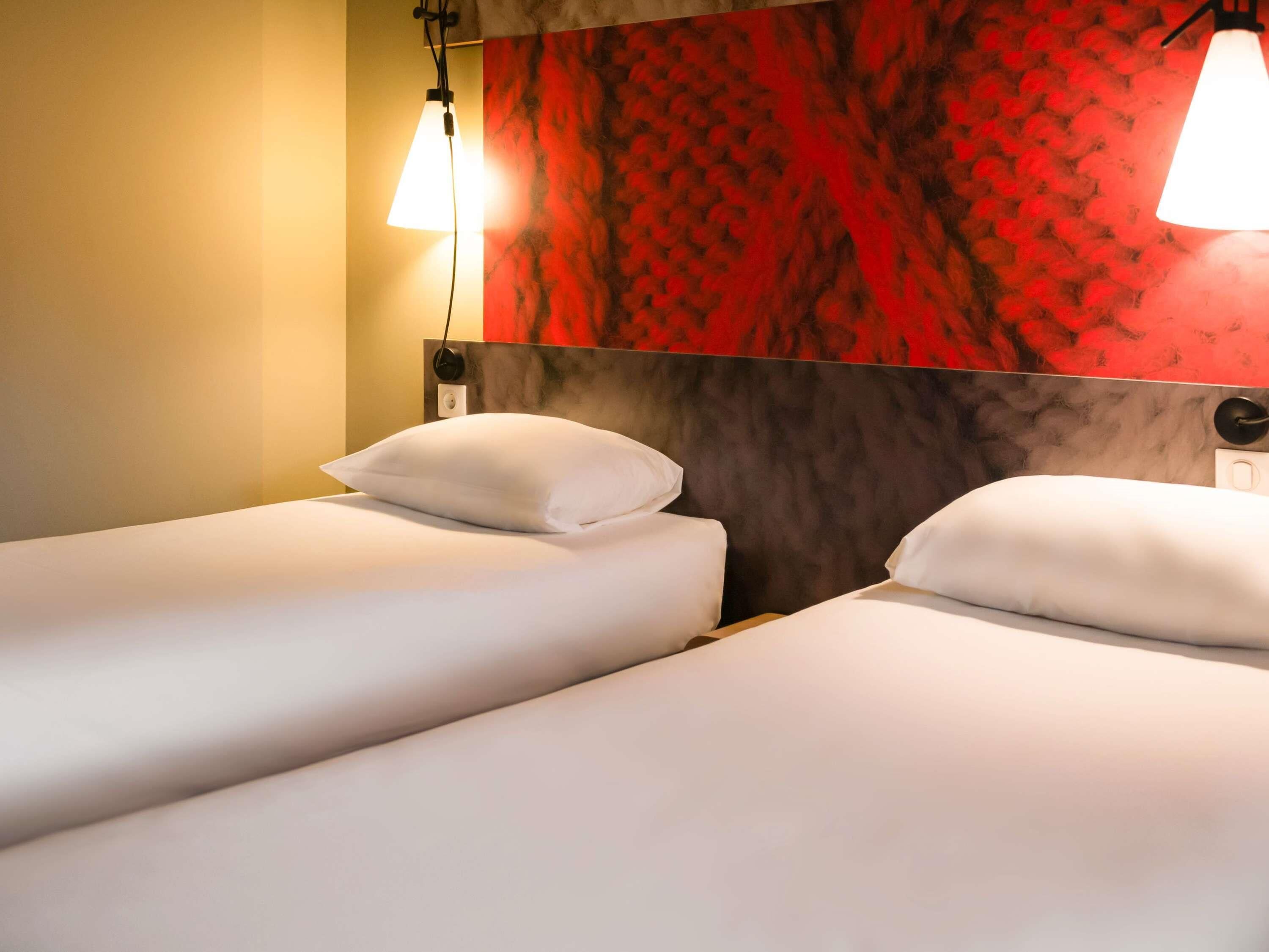 Habitación de hotel con dos camas individuales, un cabecero rojo estampado y dos lámparas colgantes.