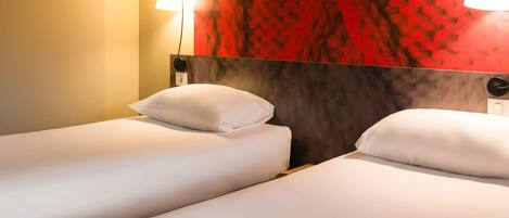 Habitación de hotel con dos camas individuales, un cabecero rojo estampado y dos lámparas colgantes.