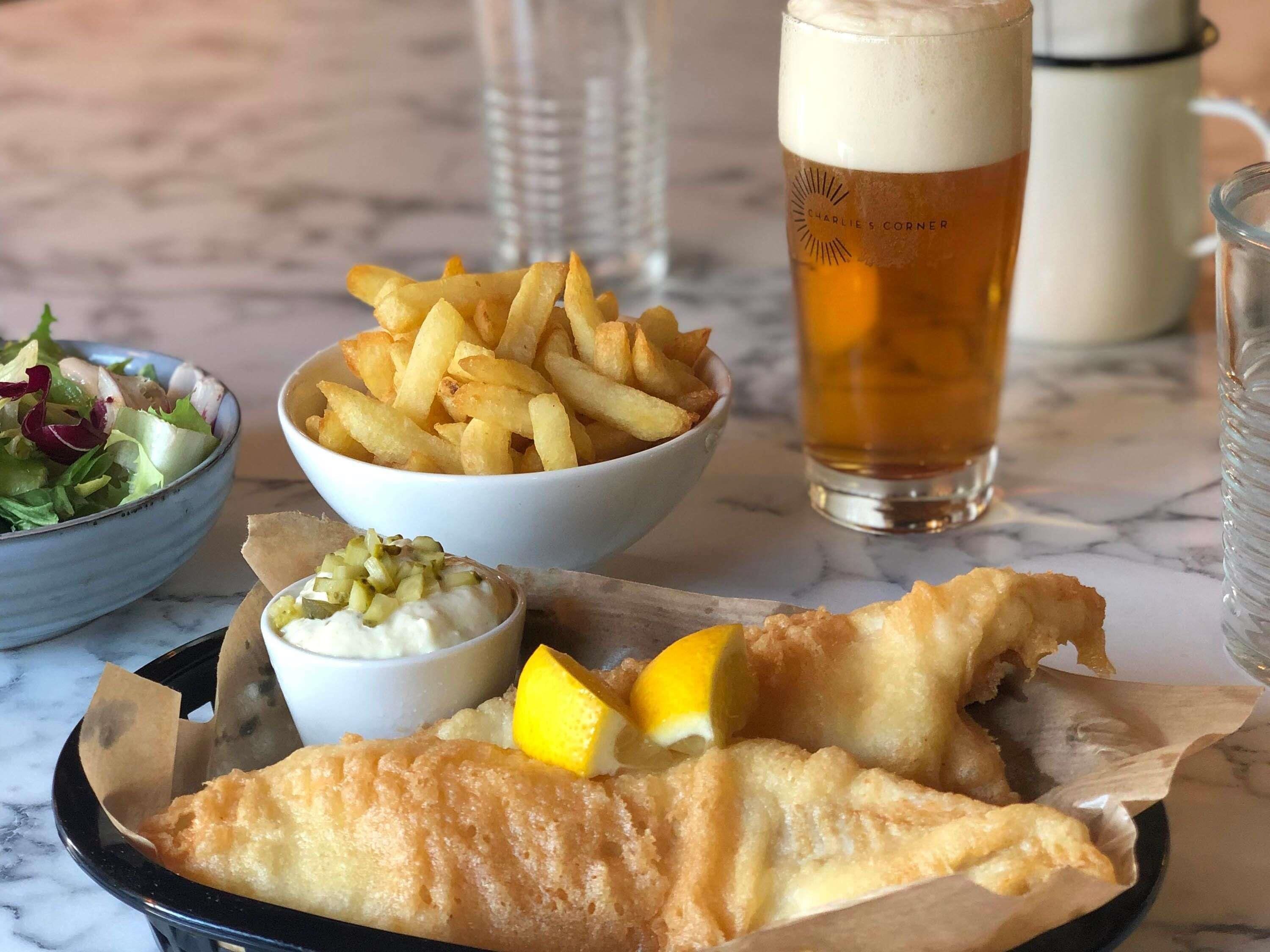 En måltid bestående av fisk och pommes frites, en sallad och en dryck, serverad på ett bord av marmor.