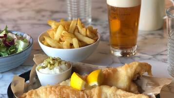 En måltid bestående av fisk och pommes frites, en sallad och en dryck, serverad på ett bord av marmor.
