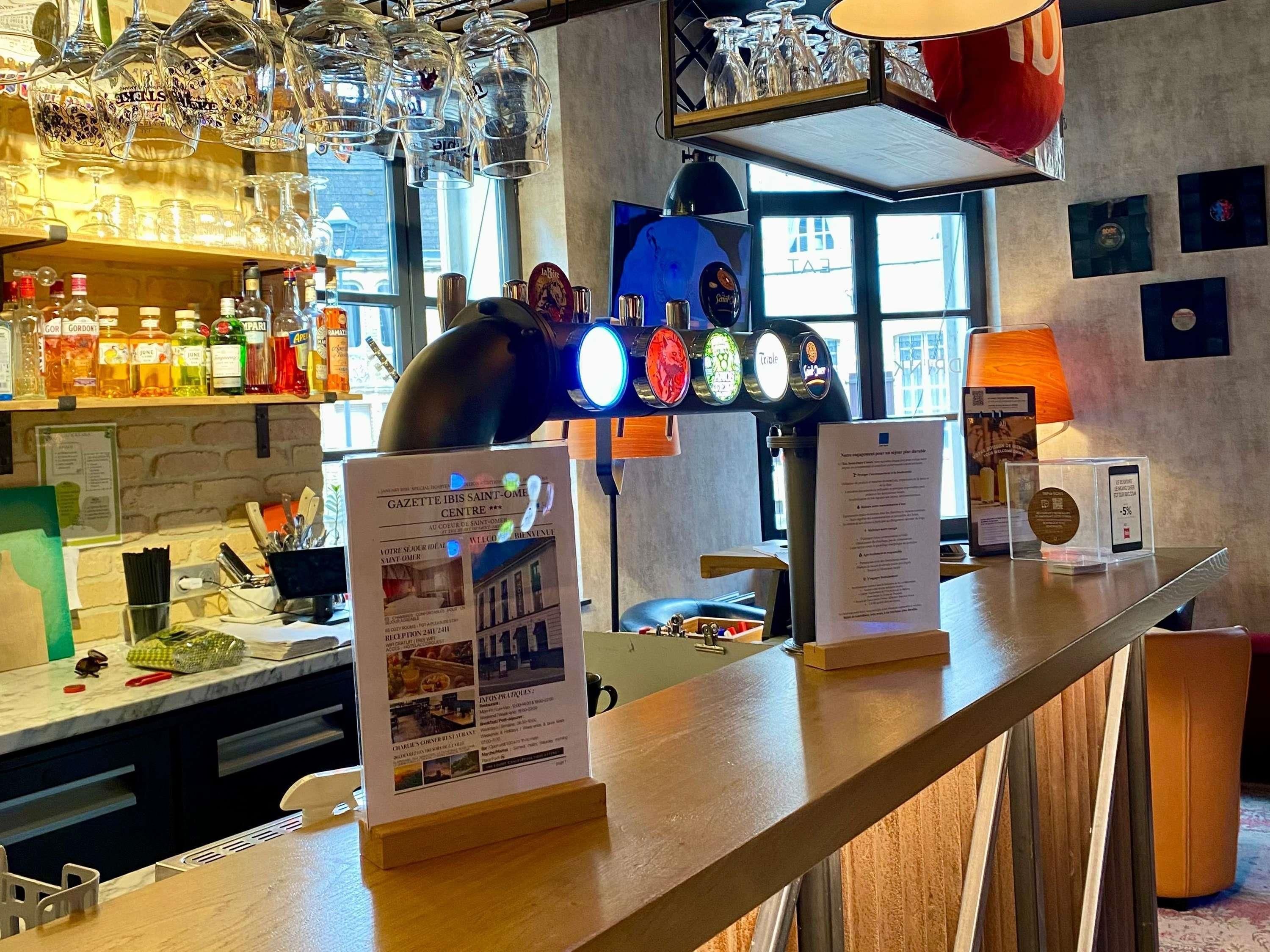 Un espace bar avec un présentoir à menus, des tabourets de bar et une variété de bouteilles exposées sur des étagères.