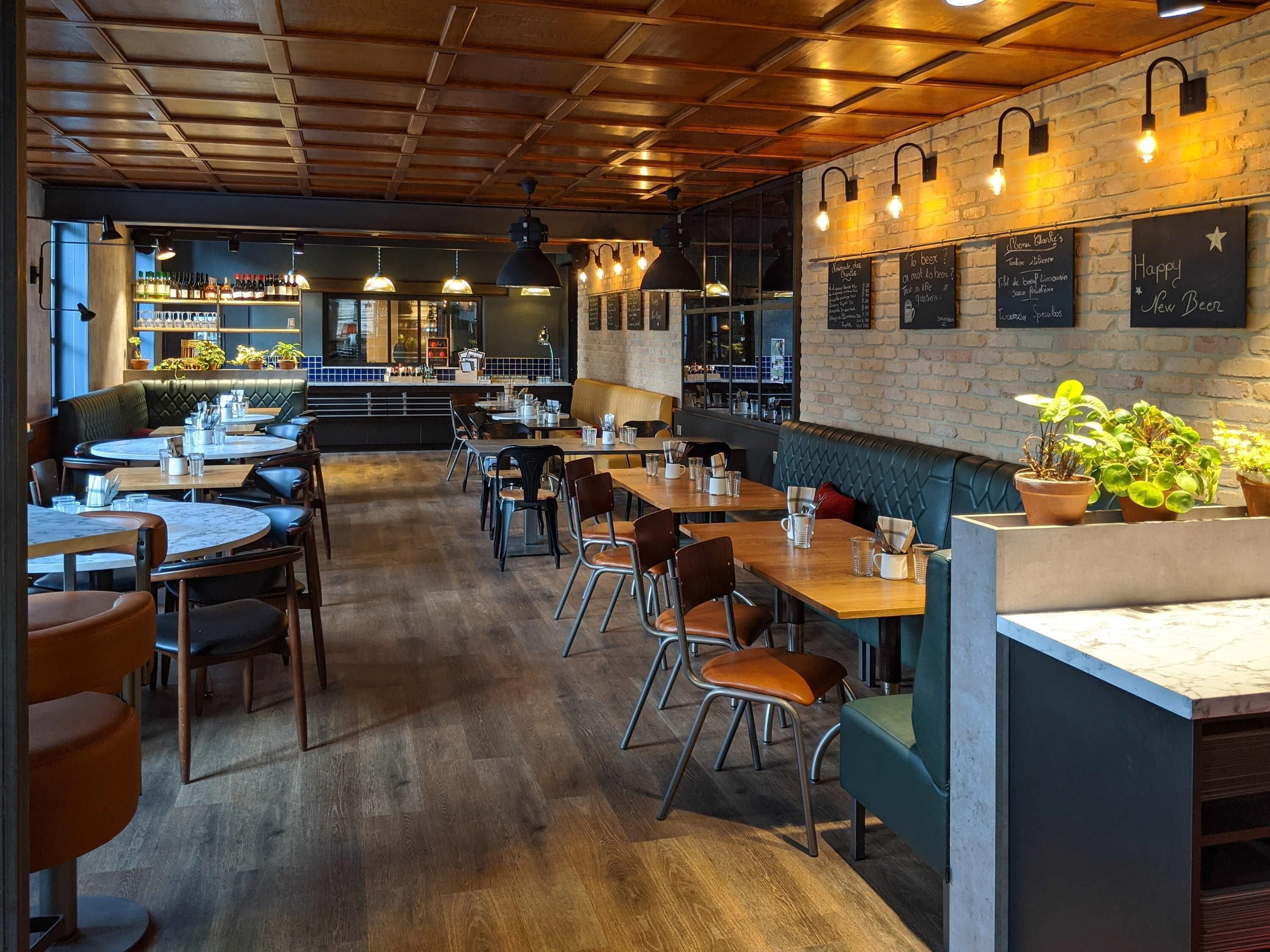 Een restaurantinterieur met houten vloeren, tafels, stoelen en een bakstenen muur met krijtbordmenu's.