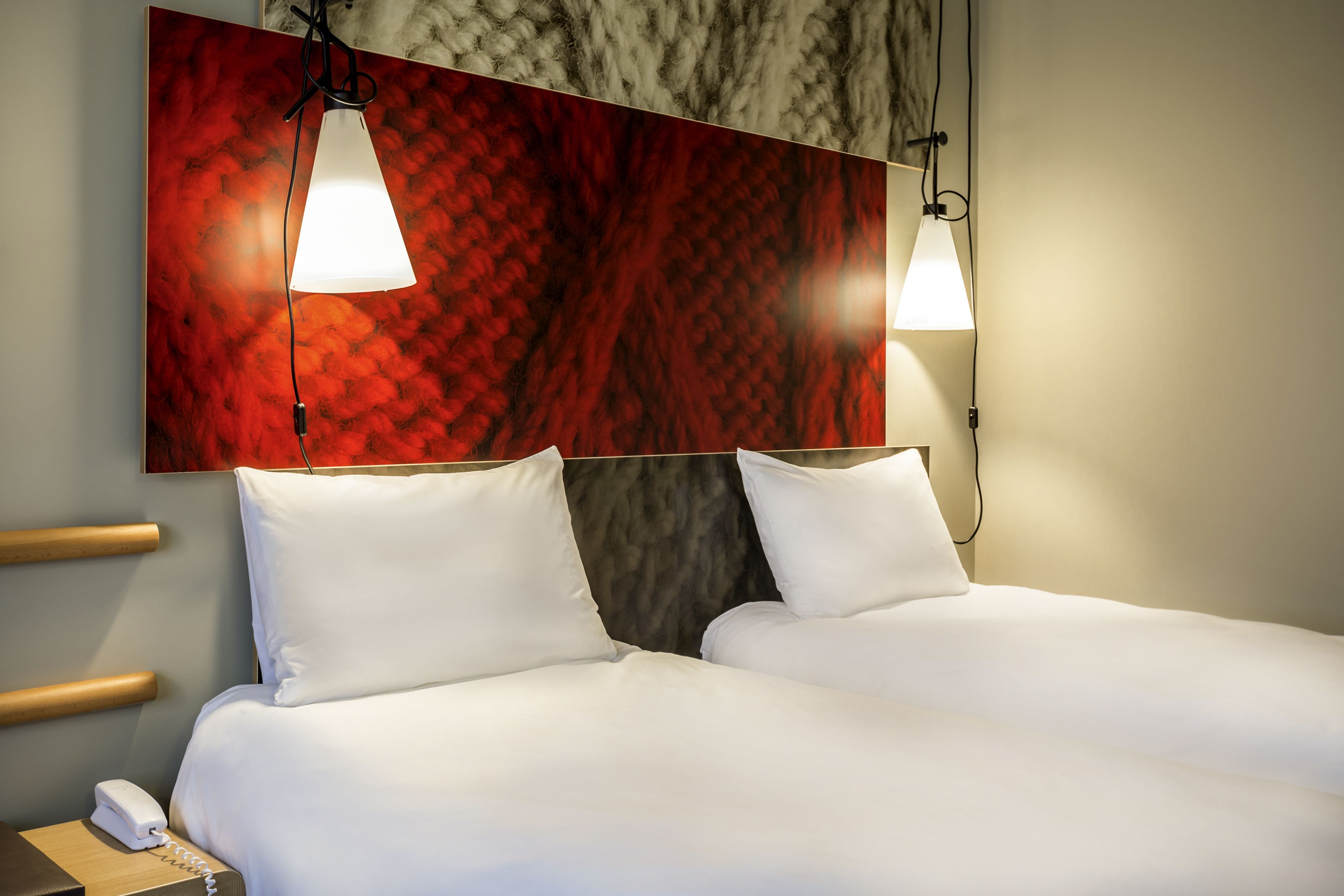 A hotel room with two beds, a marble-patterned wall, and pendant lights.
