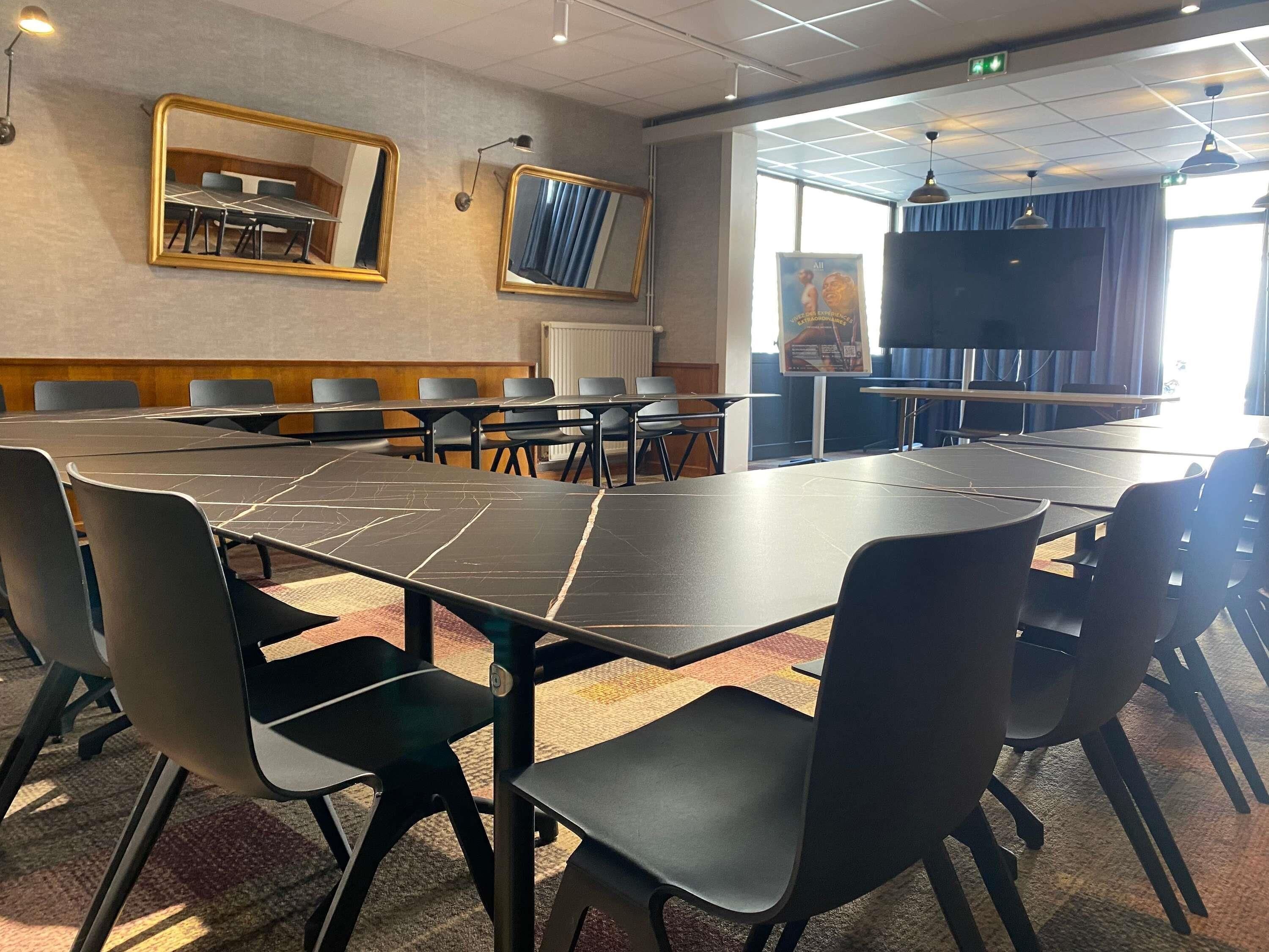 Uma sala de conferências com uma mesa grande, cadeiras e um ecrã.