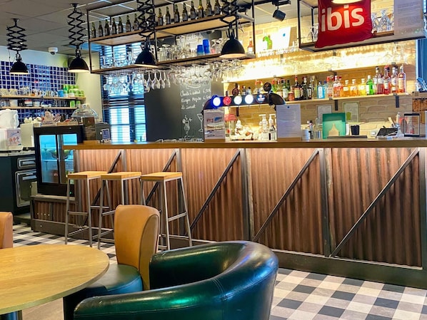A bar area with stools, a counter displaying drinks, and a menu board.