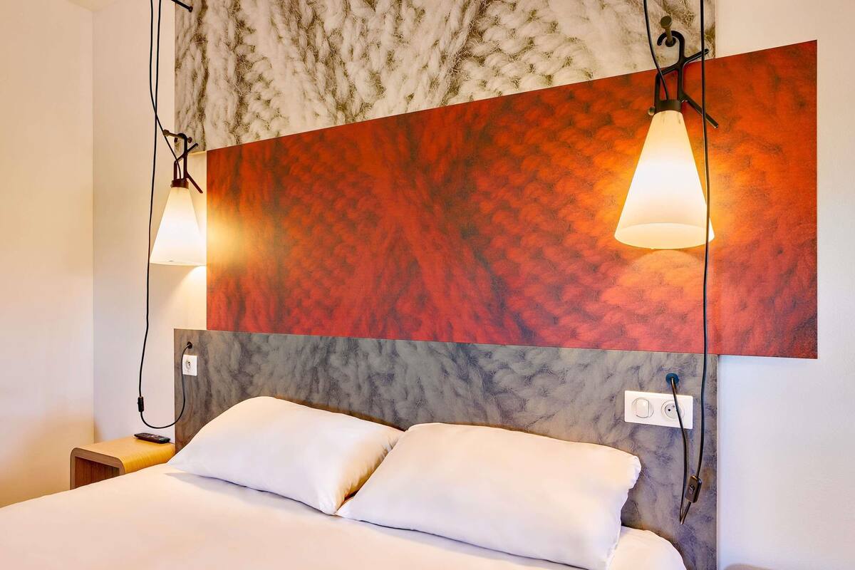 Habitación de hotel con cama, dos lámparas de noche, cabecero de mármol y pared con textura.