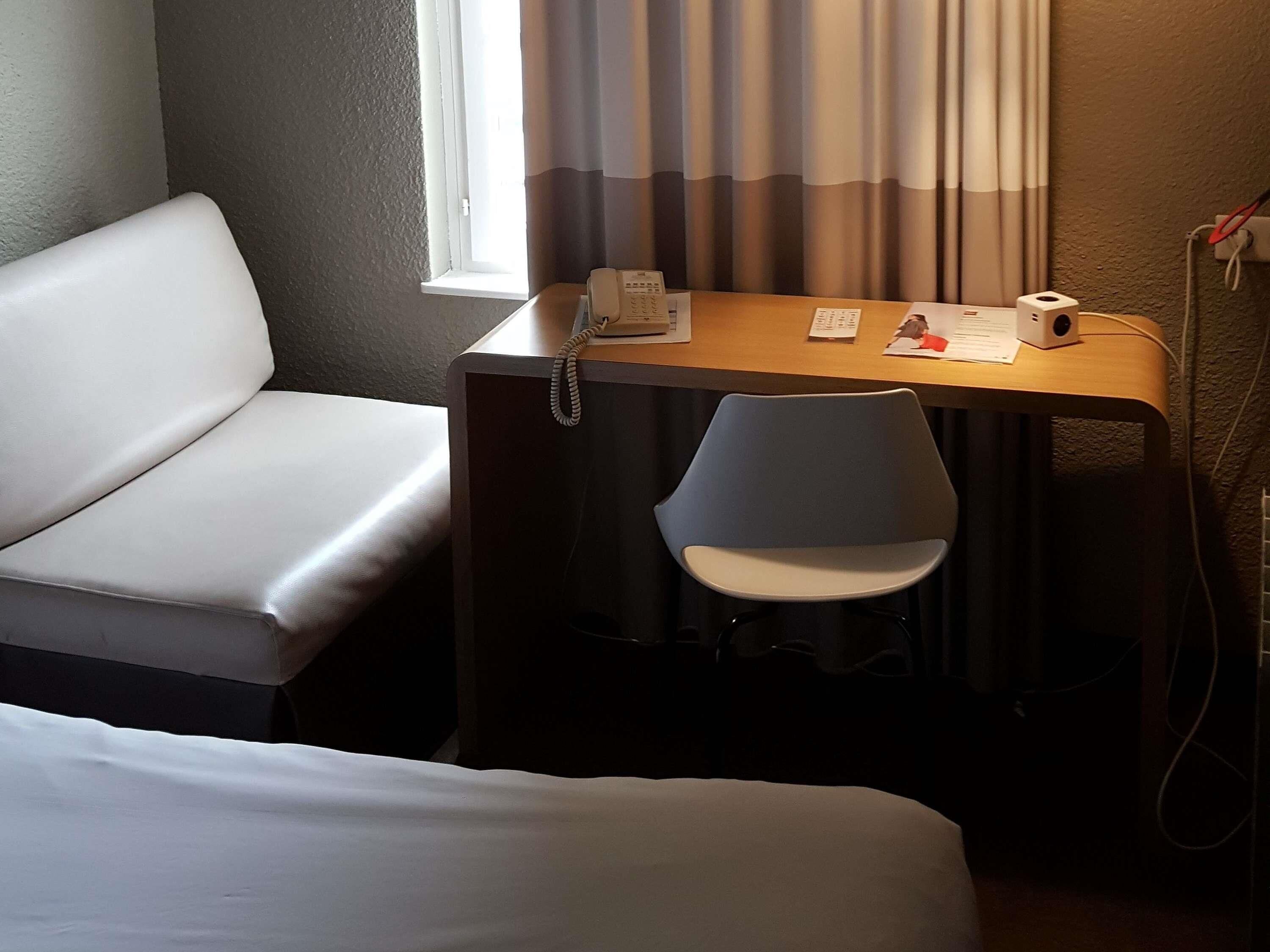 Habitación de hotel con cama, escritorio con teléfono, silla y ventana con cortinas.