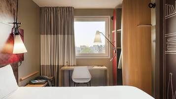 Une chambre d’hôtel comprenant un lit, un bureau avec une chaise, une lampe, une fenêtre avec des rideaux et une vue sur la ville.
