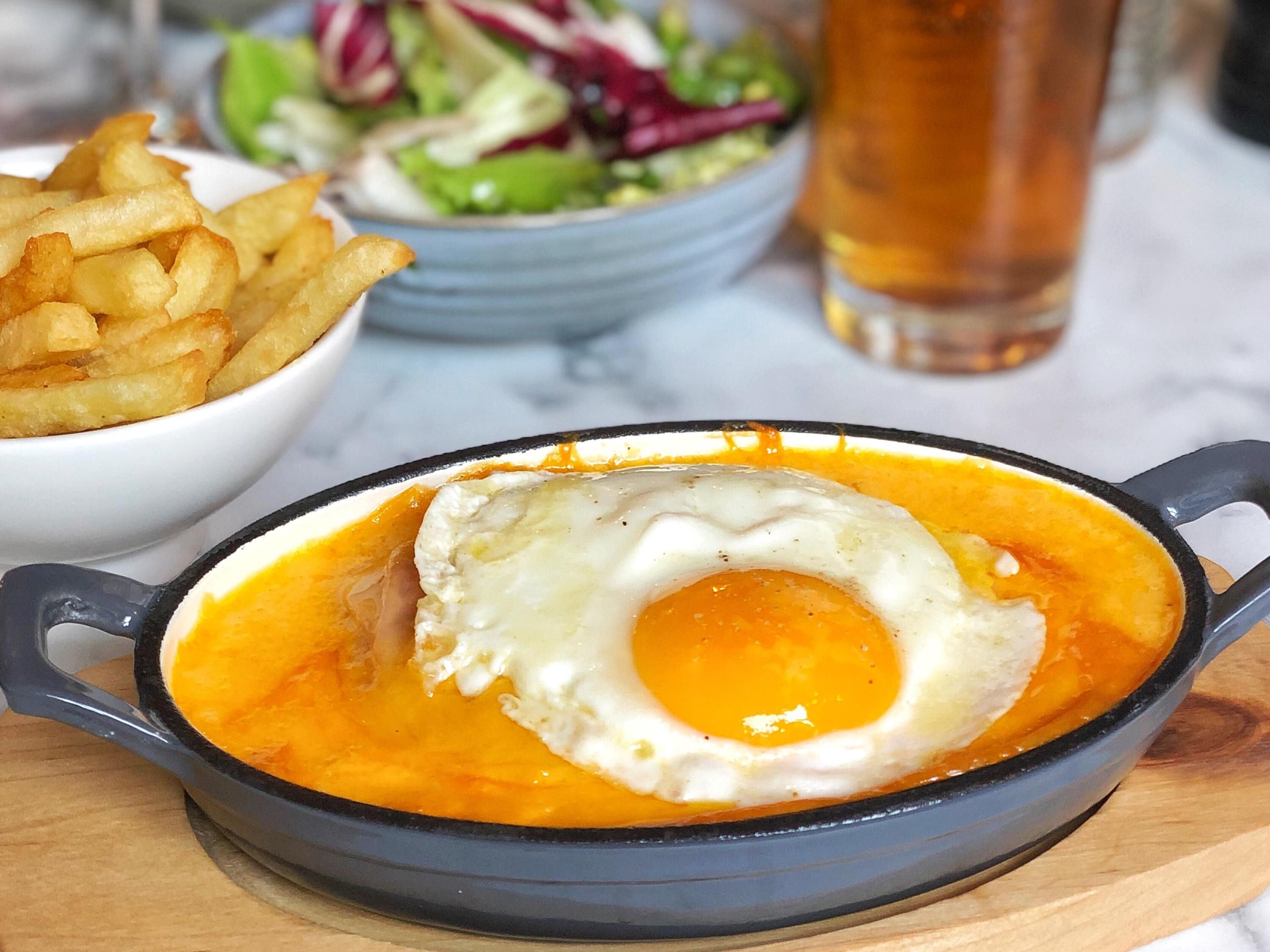 Un plat du petit-déjeuner composé d’un œuf au plat servi dans une poêle, accompagné de frites et d’une salade.