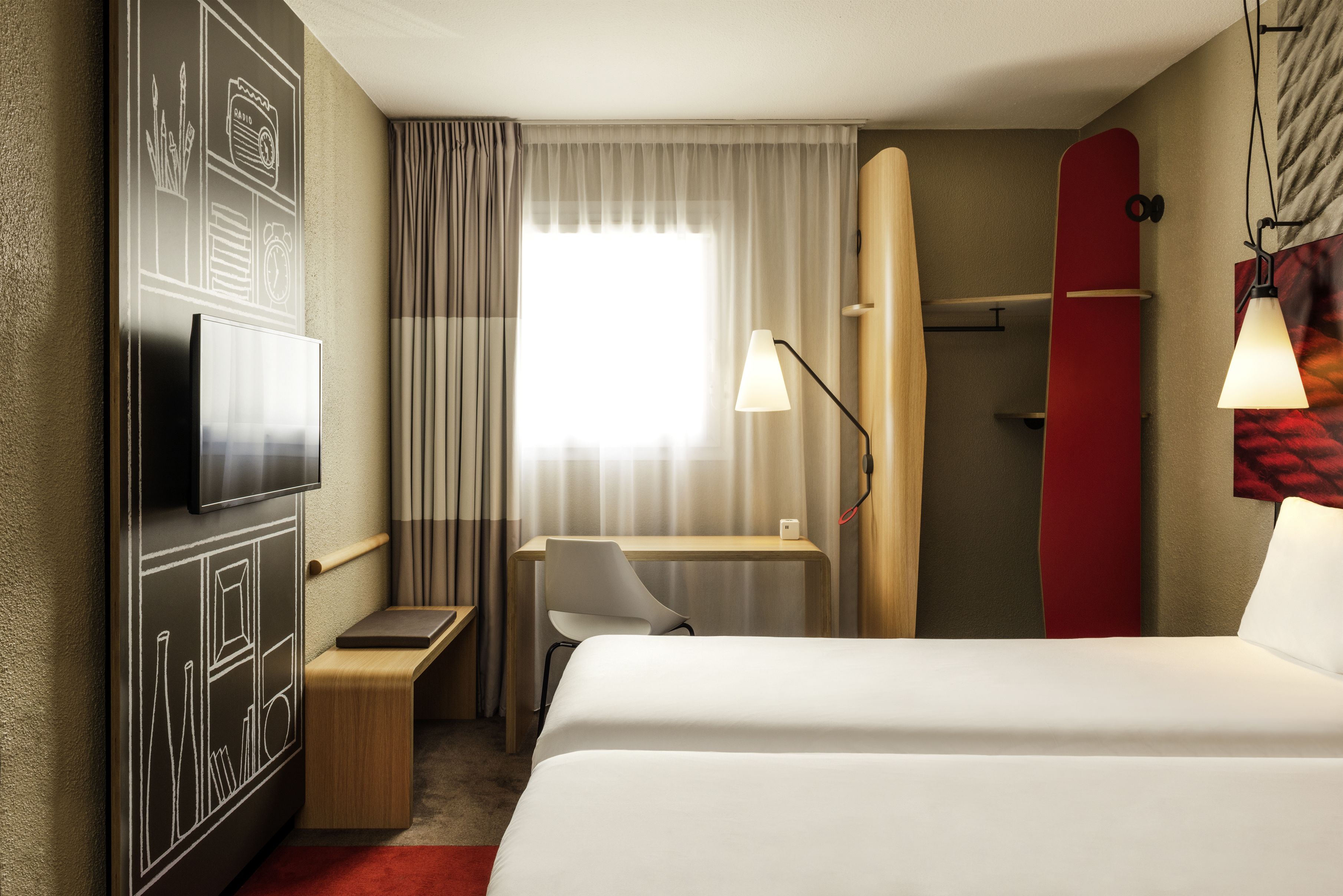 A hotel room with a bed, desk, chair, TV, and a surfboard.