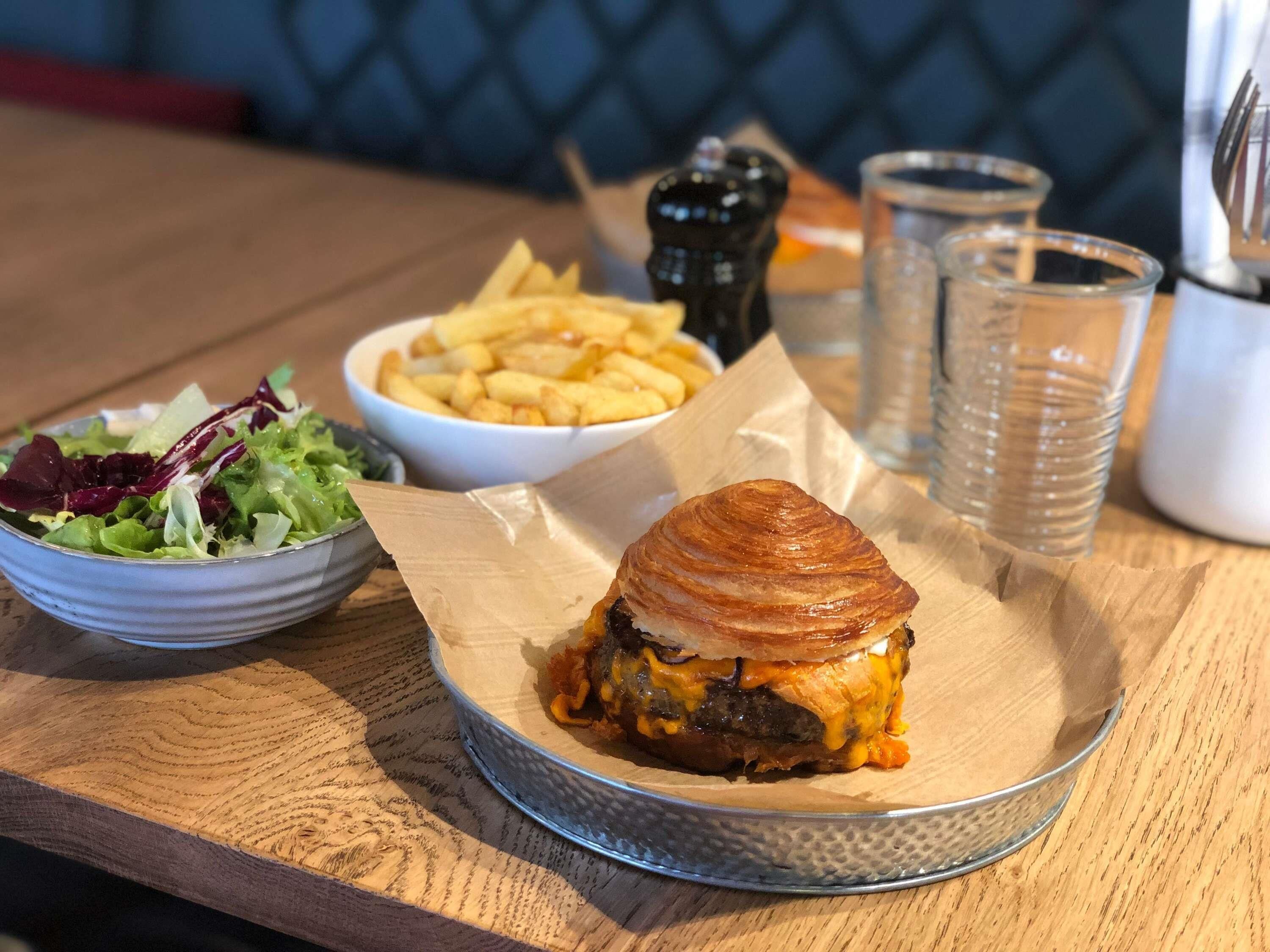 Una comida con hamburguesa, papas fritas y ensalada sobre una mesa de madera.