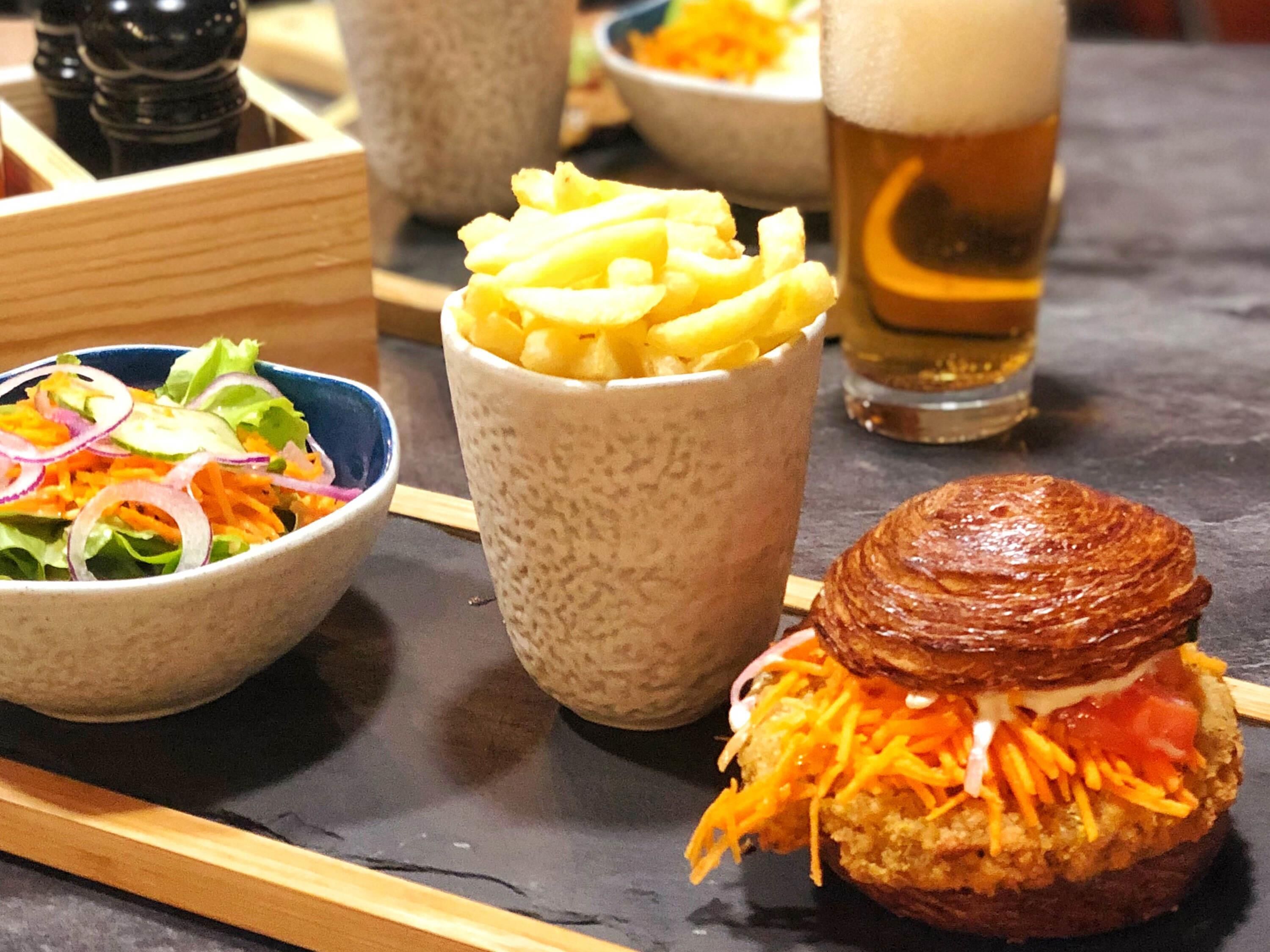 Una comida con una hamburguesa, papas fritas y una ensalada sobre una mesa.