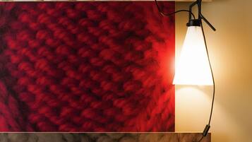 Una cama con ropa de cama blanca, una pared texturizada de color rojo y una lámpara fijada a la pared.